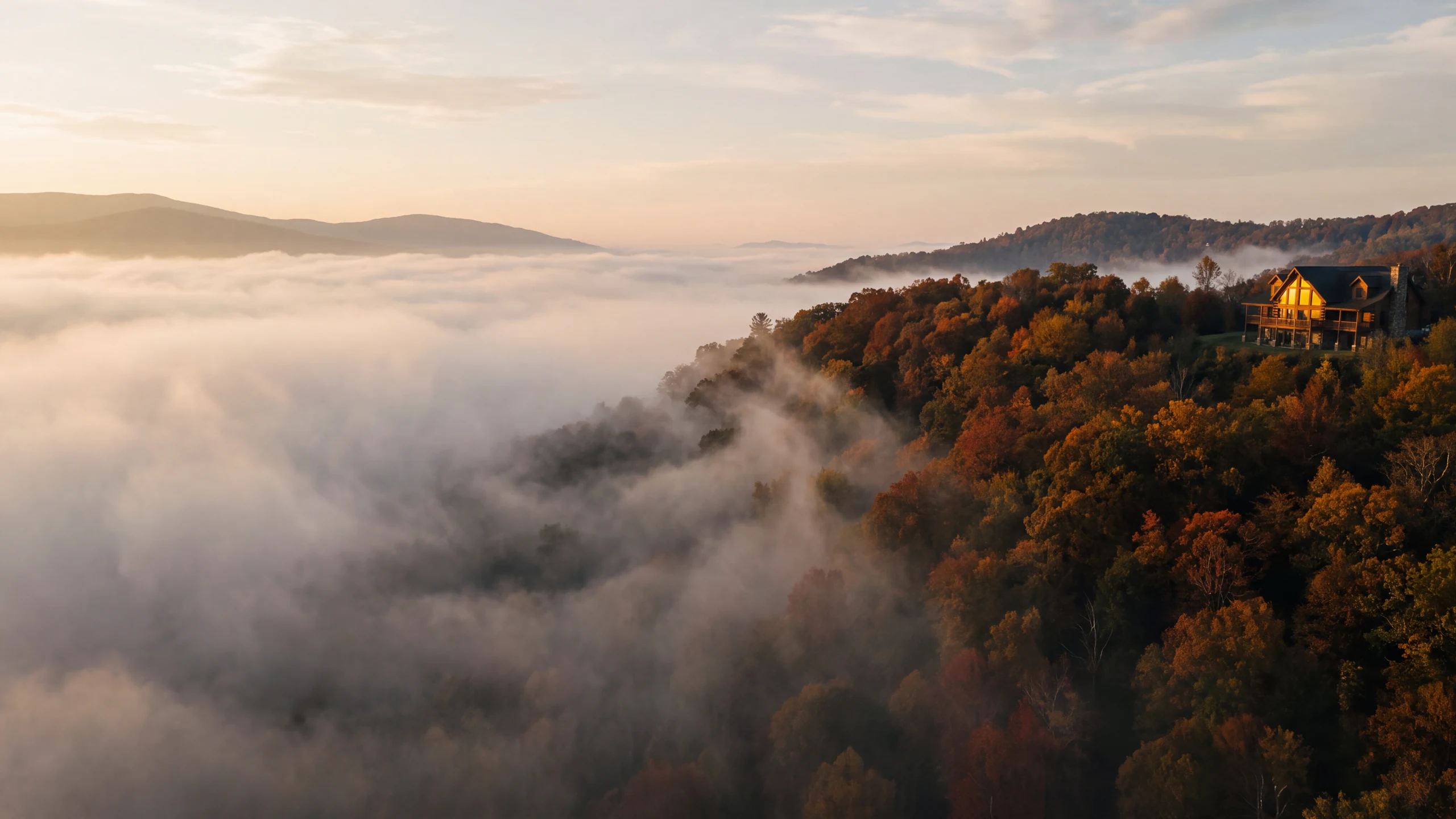 Dawn over a fog filled Blue Ridge valley, a lit timber cabin on the autumn ridge